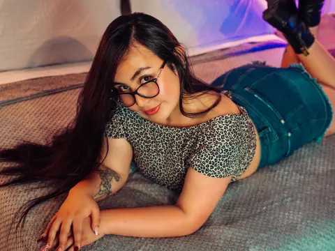 Young woman with glasses in a leopard print top and denim shorts relaxing on a bed in soft mood lighting.