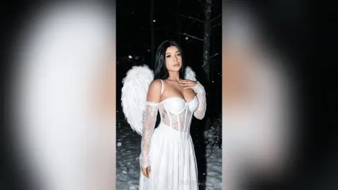 Ethereal woman in a white lace angel costume with large wings posing in a snowy winter forest at night.