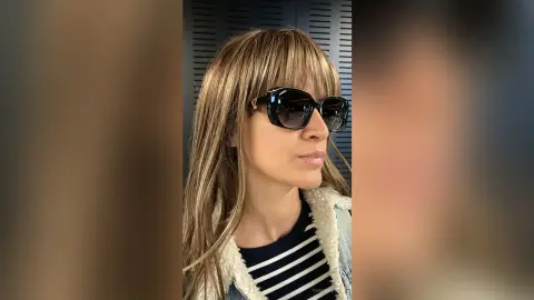 Stylish woman with blonde hair and sunglasses wearing a cozy white fleece jacket in a modern indoor setting.
