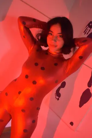Young woman in a red polka dot bodysuit posing under warm red lighting for a moody aesthetic portrait.