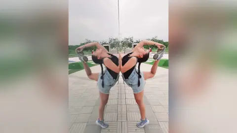 Athletic woman in a black tank top and denim shorts performing a flexible yoga stretch outdoors.