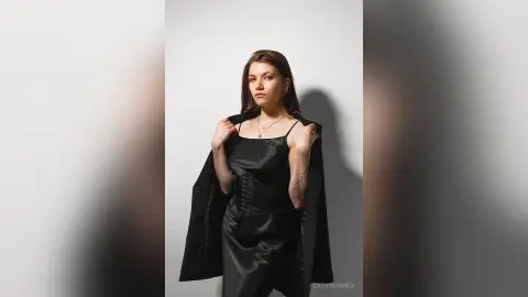 Elegant woman in a black satin slip dress and corset posing against a minimalist studio background.