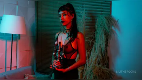 LilithBrooks poses in a black sheer bodysuit, looking forward while holding a hookah pipe against a background of blinds and pampas grass.