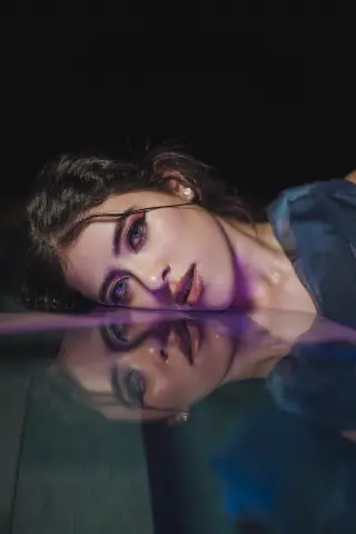 Close-up portrait of a woman with dramatic makeup reflecting in water for a moody, ethereal aesthetic.