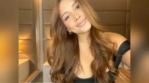 Smiling brunette woman in a black top posing in a warm, cozy indoor setting.