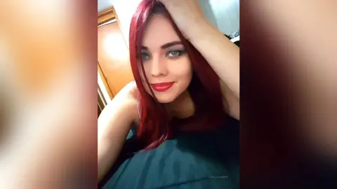 Smiling woman with vibrant red hair wearing a black top in a bright indoor setting.