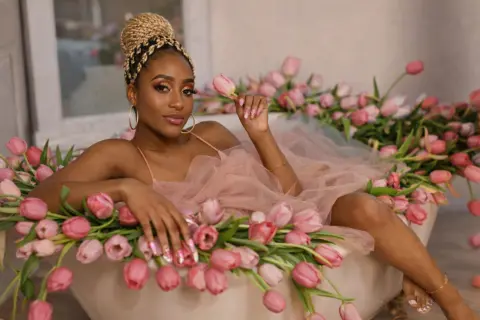 Beautiful Black woman in a pink tulle dress relaxing in a bathtub filled with pink tulips, dreamy romantic mood.
