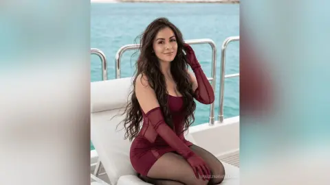 Elegant woman in a burgundy sheer dress relaxing on a white yacht overlooking the turquoise ocean.