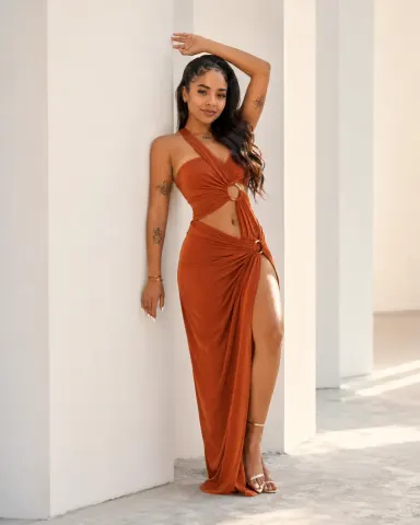 ScarlettPearls — ScarlettPearls poses in a long rust-colored cutout dress against a white wall.