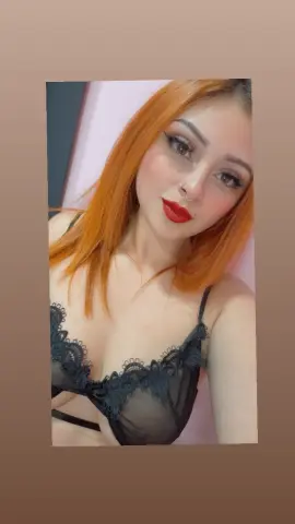 Redheaded woman in black lace lingerie posing with a glamorous makeup look in a soft indoor setting.