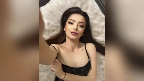 Young woman with long dark hair wearing a black lace camisole relaxing on a white faux fur rug.
