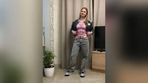 SilviaPrespertys stands in a room wearing a pink crop top, an open black jacket, and baggy grey jeans.