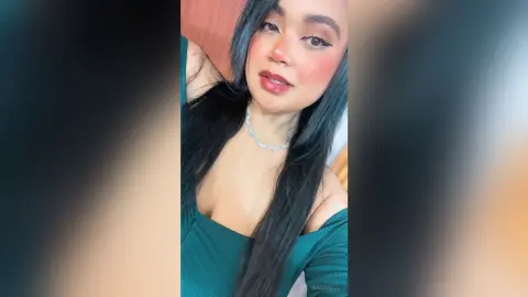 NiaCorelli poses with long black hair and a silver necklace, wearing a low-cut dark green top.