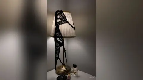 Hailey's black lace panties hanging off a lamp shade next to a bottle of perfume on a white table.