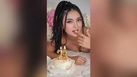 Young woman with long braids celebrating her 23rd birthday with a white cake in a soft, dreamy setting.