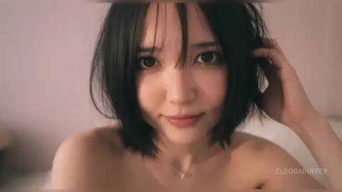 Smiling young woman with short black hair wearing a delicate silver necklace in soft, warm lighting.