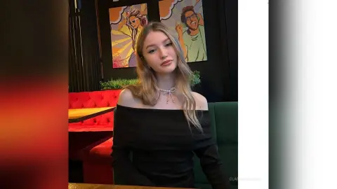 Blonde woman in a black off-the-shoulder top sitting in a modern cafe with colorful wall art.