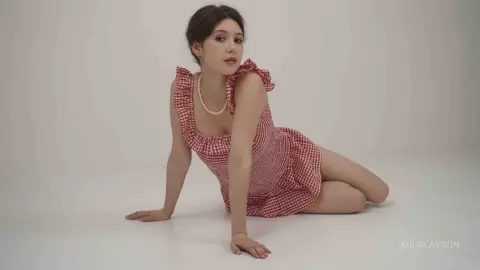 Young woman in a red gingham sundress sitting on a white floor with a soft, minimalist aesthetic.