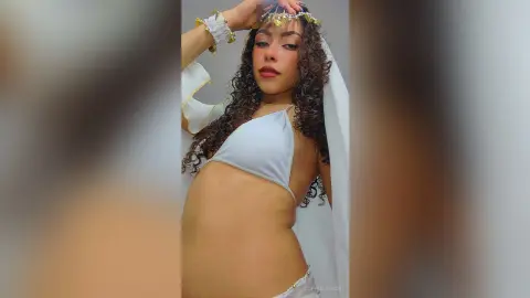 Young woman in white goddess outfit and gold headpiece posing with a serene expression.