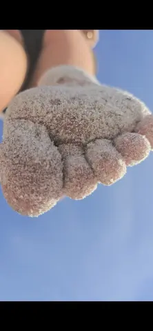 Close-up of a person's bare foot covered in white sand against a clear blue sky summer beach background.