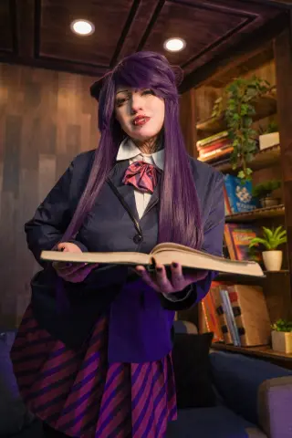 Cosplayer in purple anime school uniform holding an open book in a cozy library setting.
