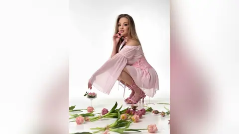 Elegant woman in a pink off-the-shoulder dress posing with tulips in a bright, dreamy studio setting.