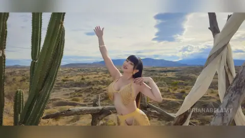 Smiling woman in a yellow bikini posing in a sunny desert landscape with cacti and mountains.