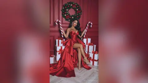 AnnaKarev poses in a red dress and high heels, holding candy canes next to white Christmas presents.