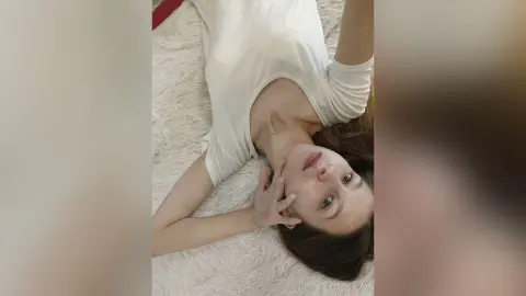 Young woman in a white casual top relaxing on a soft white textured rug in a bright, serene indoor setting.
