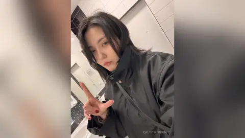 Young woman with dark hair wearing a black jacket in a modern bathroom setting with a moody aesthetic.