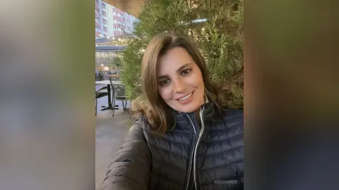 Smiling woman in a black puffer jacket relaxing at an outdoor cafe setting.