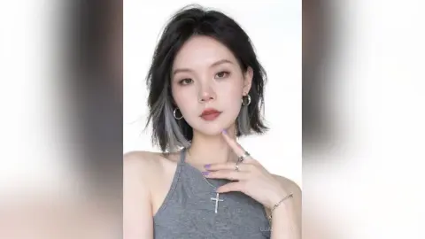 Portrait of a young woman with wavy grey hair wearing a grey tank top and silver cross necklace against a white background.