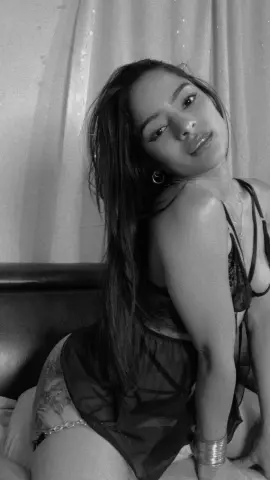 Black and white portrait of a woman in a black lace bodysuit posing indoors with a moody aesthetic.