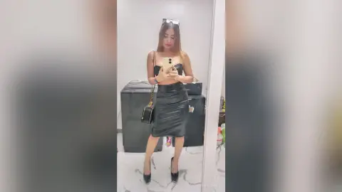 Young woman in a chic black strapless top and leather skirt taking a mirror selfie in a modern room.