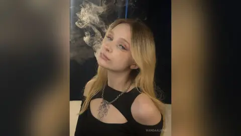 Blonde woman in a black cutout top posing with smoke in a moody, cinematic indoor setting.