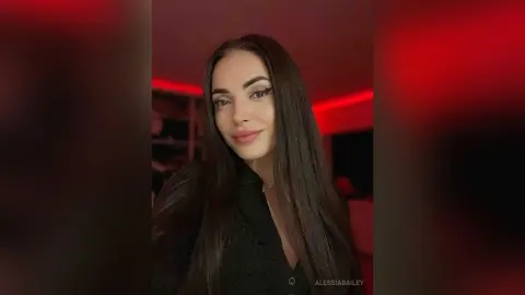 Beautiful woman with long dark hair wearing a black outfit in a moody room with red neon lighting.