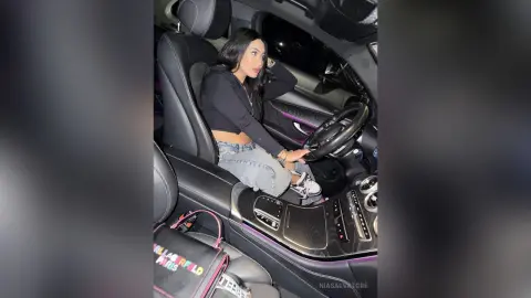 Young woman in a black crop top and jeans sitting in a luxury car interior at night.