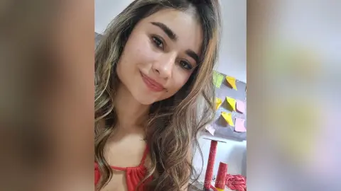 CrystallRosse smiles for a selfie, wearing a red top with her long brown hair flowing over her shoulders.