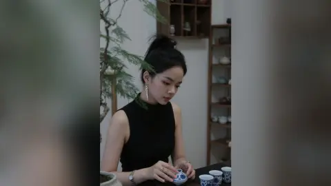 Young woman in a black sleeveless top enjoying a peaceful tea ceremony in a cozy indoor setting.