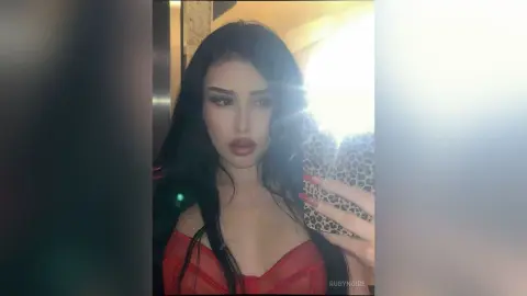Glamorous woman with long dark hair wearing a red outfit in a brightly lit indoor setting.