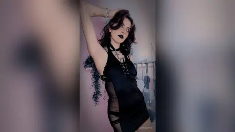LorenLoiss poses with one arm raised, wearing a black lace-up teddy and a black choker.