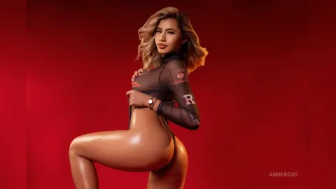 Glamorous blonde woman in a black sheer bodysuit posing against a bold red studio background.
