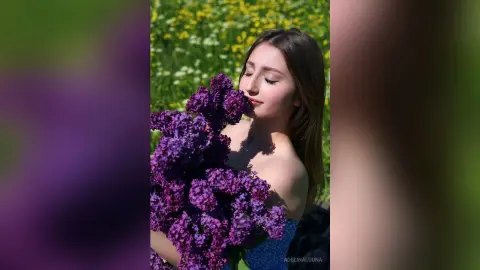 Young woman in a black dress holding a large bouquet of purple lilacs in a sunny spring meadow.