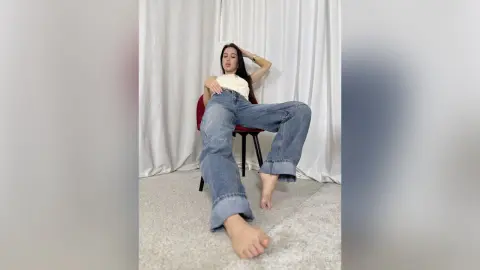 Young woman in casual denim jeans and white top posing relaxed in a bright indoor setting.