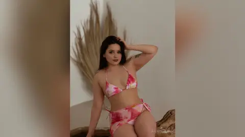 Young woman in a pink floral bikini posing confidently in a minimalist bohemian studio setting.