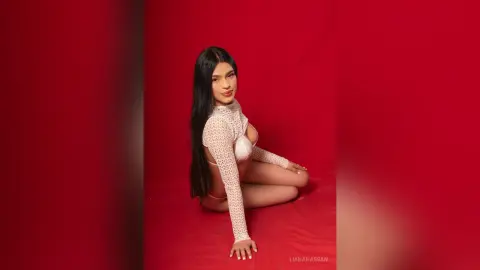 Young woman in a white lace long-sleeve top sitting against a vibrant red background with a moody aesthetic.