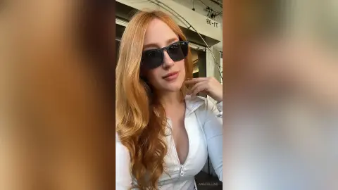Redheaded woman in a white zip-up top and sunglasses posing outdoors with a confident, stylish mood.