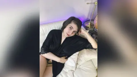 Young woman in a black satin robe relaxing on a white sofa in a dimly lit room.