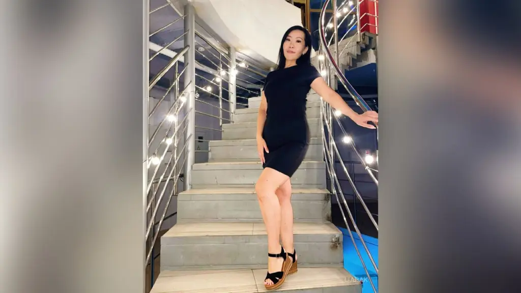 Elegant woman in a black dress standing on modern indoor stairs with bright decorative lights.