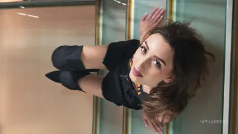 IvyHarpers poses with her hands behind her head, wearing a black tank top and black shorts against a light background.